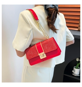 Detail of red crossbody bag featuring glitter flap and gold metal chain strap on model