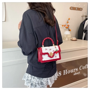 Crossbody bag with cherry print, red woven handle, and gold floral clasp detail