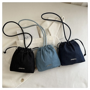 Three colors of denim drawstring bucket bags with metal logos on white corduroy