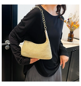 Detail of woven straw hobo bag featuring a bold gold chain strap and textured finish