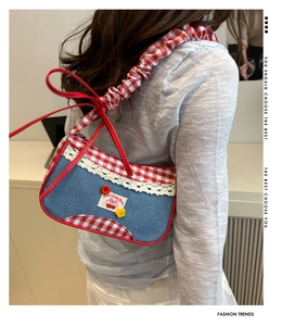 Detail of a denim shoulder bag with red plaid trim and cherry embroidery on a model