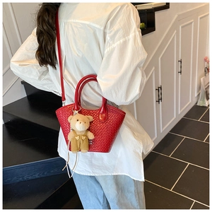 Detail view of red woven texture bucket bag with a cute bear charm on a female model