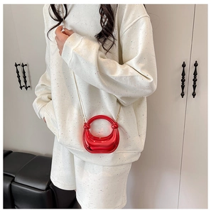 Close-up of a glossy red circular mini handbag featuring an elegant gold metal chain strap