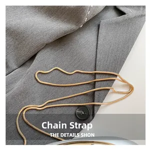 Macro view of a polished gold snake chain shoulder strap on grey fabric detail