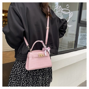 Detail view of pink crocodile texture handbag with gold lock and decorative scarf on handle