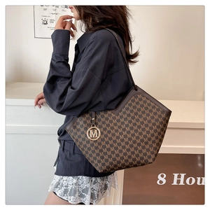 Detail of brown tote bag with M-letter monogram pattern and gold metal pendant