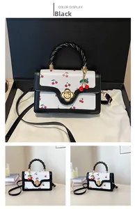 Detailed view of white cherry print handbag with black flap and gold floral lock in gift box