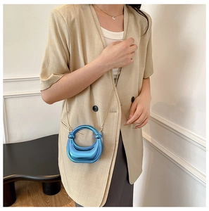 Glossy metallic blue horseshoe shoulder bag with gold chain strap on beige blazer
