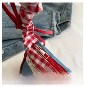 Close-up of smooth metal zipper and lace trim on a red checkered denim crossbody bag
