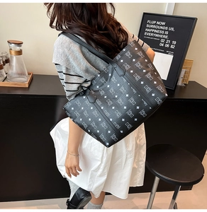 Detail of large black tote bag with monogram bear print shown on a model's shoulder