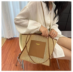 Detailed view of beige straw tote bag with brown leather trim and luxury gold lettering