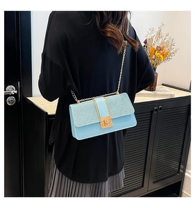 Close-up of light blue glitter crossbody bag with gold chain strap on shoulder