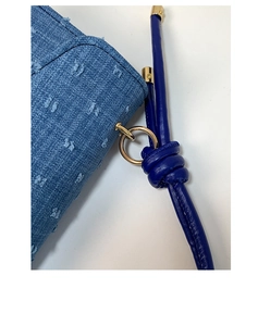 Close-up detail of blue denim handbag featuring a knotted strap and gold hardware
