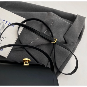 Close-up of minimalist black leather crossbody bag with textured gold metal lock and strap detail