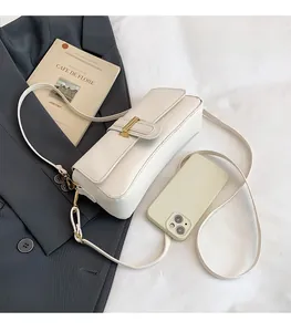 Detail view of cream rectangle crossbody bag with gold buckle and smartphone for scale