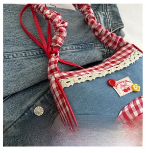 Close-up of denim shoulder bag with red plaid trim, lace edges, and cherry embroidery