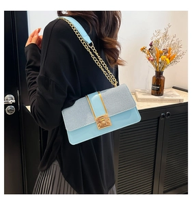 Detail showing gold chain strap and metallic lock on light blue textured crossbody bag