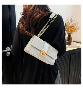 Detail of elegant cream shoulder bag with metallic chain strap worn by a model