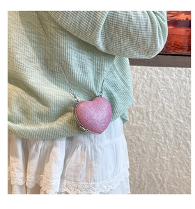 Dettaglio di una borsa rosa a forma di cuore con catena d'argento indossata in vita da una modella