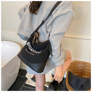 Détail du sac seau en toile noire avec base en cuir et logo contrasté blanc