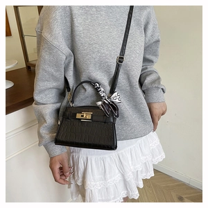 Detail of black crocodile-embossed leather handbag with gold metal lock and silk scarf wrap