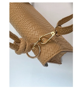 Gros plan sur la boucle dorée et la bandoulière tressée d'un sac à main beige