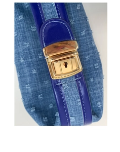 Close-up detail of a denim crossbody bag with a gold metal buckle and purple strap.
