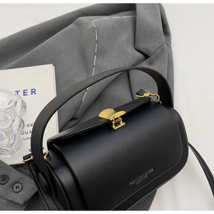 Close-up of black leather crossbody bag with elegant golden fan-shaped buckle clasp