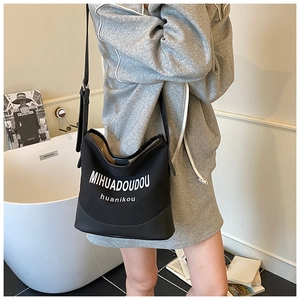 Détail du sac seau en toile noire et cuir avec typographie blanche et bandoulière réglable