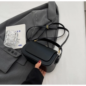 Detail view of minimalist black leather crossbody bag with elegant gold hardware and strap