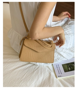 Vue détaillée d'un sac bandoulière tissé kaki tenu par une femme en robe blanche chic