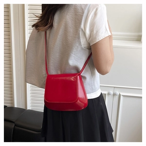 Detailed view of a bright red glossy leather saddle bag worn by a model in casual style