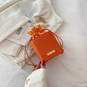 Mini sac seau orange avec cordon et chaîne dorée sur tissu en tweed blanc