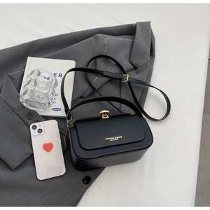 Detail of matte black square crossbody bag with gold buckle on grey blazer backdrop