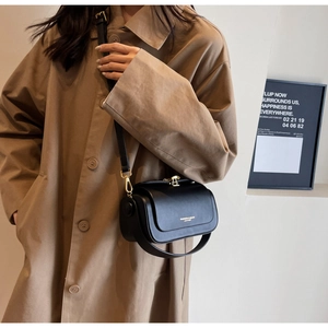 Detail of minimalist black leather crossbody bag with gold metal buckle on khaki coat