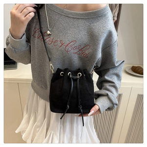 Detail of black suede drawstring bucket bag with gold eyelets worn by a model