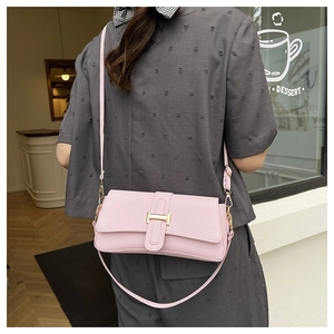 Close-up of light pink crossbody bag featuring a golden H-buckle and textured leather