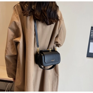 Detail of a black matte leather crossbody bag with gold hardware on a trench coat