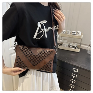 Detail of dark brown leather crossbody bag featuring vintage V-shaped rivet patterns