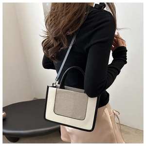 Detail of a two-tone canvas and leather tote bag showing crossbody strap and contrast piping