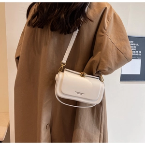 Detail of white leather crossbody bag with gold metallic buckle on a model wearing a coat