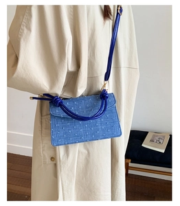 Detailed view of a blue denim crossbody bag featuring unique knotted strap design.