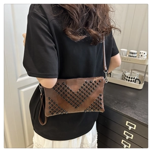 Detail of brown leather crossbody bag with black rivets on a model in a home setting