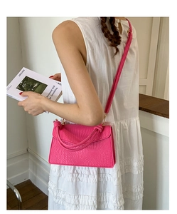 Sac bandoulière rose fuchsia à texture tressée porté élégamment sur robe blanche