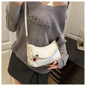 Détail du sac croissant en cuir blanc avec chaîne dorée et breloque cerise