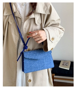 Detail shot of blue textured crossbody square bag worn with a beige trench coat
