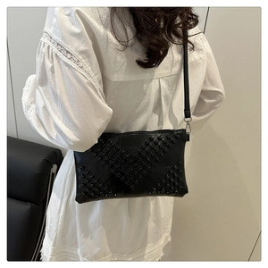 Detail of black crossbody bag with V-shaped rivet studs on white shirt background