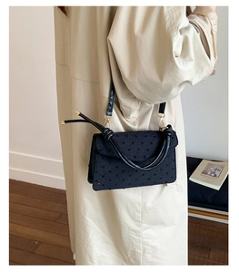 Detailed side view of vintage black textured small crossbody bag worn on a beige coat