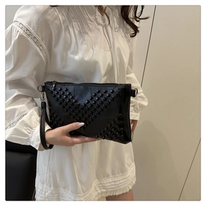 Detail of black envelope clutch with rivet studs and V-shaped patterns on leather surface