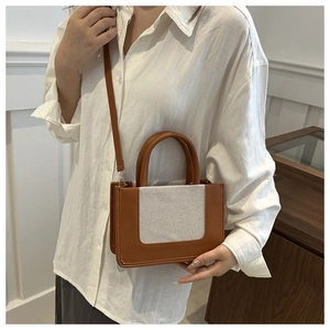 Detail of a brown leather and beige canvas paneled tote bag with detachable strap